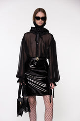 Model wearing the Helen Anthony black organza neck frill with detachable satin flower tie, styled with a sheer black silk organza shirt, PU-coated high shine leather skirt and small shoulder black leather bag
