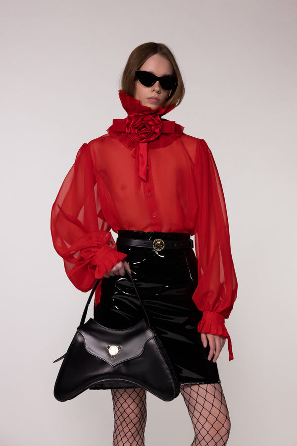Model wearing the Helen Anthony red organza neck frill with detachable satin flower tie, styled with a sheer red silk organza shirt, PU-coated high shine leather skirt and black leather small shoulder bag