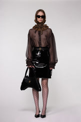 Model wearing the Helen Anthony black organza neck frill with detachable satin flower tie, styled with a sheer brown silk organza shirt, PU-coated high shine leather skirt and small shoulder leather bag