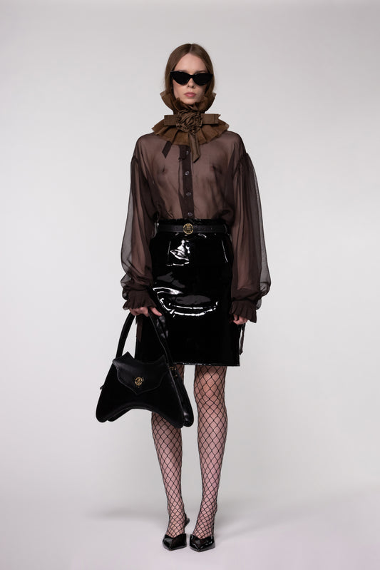 Model wearing the Helen Anthony black organza neck frill with detachable satin flower tie, styled with a sheer brown silk organza shirt, PU-coated high shine leather skirt and small shoulder leather bag