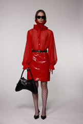 Model wearing the Helen Anthony red organza neck frill with detachable satin flower tie, styled with a sheer red silk organza shirt, PU-coated high shine leather skirt and black leather small shoulder bag