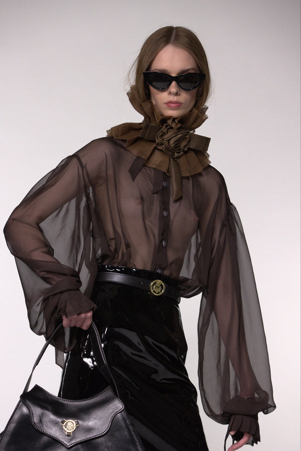Model wearing the Helen Anthony brown organza neck frill with detachable satin flower tie, styled with a sheer brown silk organza shirt and black leather small shoulder bag.