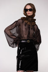 Model wearing the Helen Anthony black organza neck frill with detachable satin flower tie, styled with a sheer brown silk organza shirt and PU-coated high shine leather skirt