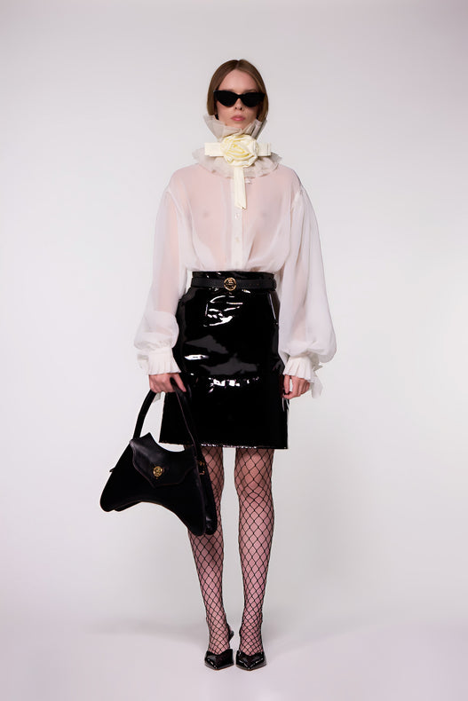 Model wearing the Helen Anthony white organza neck frill with detachable satin flower tie, styled with a sheer white silk organza shirt, and PU-coated high shine leather skirt 
