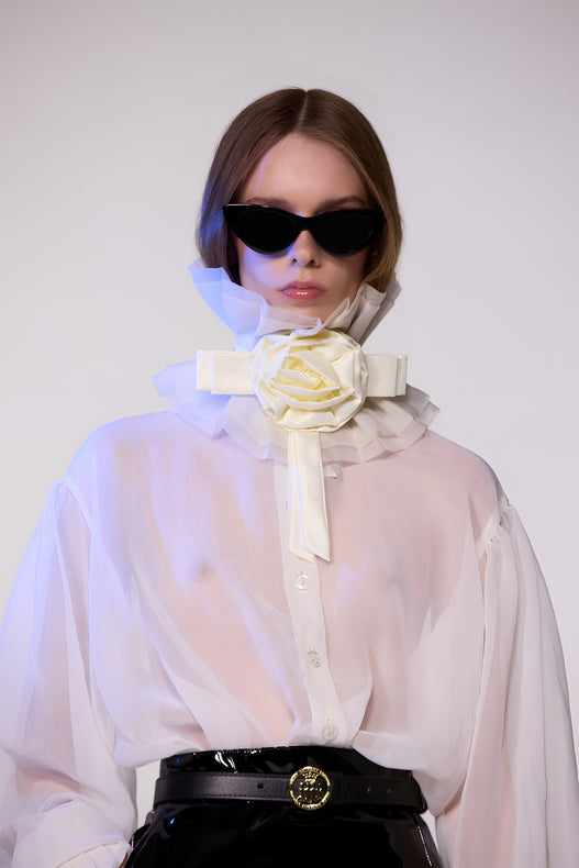 Model wearing the Helen Anthony white organza neck frill with detachable satin flower tie, styled with a sheer white silk organza shirt, and PU-coated high shine leather skirt 