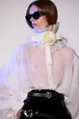 Model wearing the Helen Anthony white organza neck frill with detachable satin flower tie, styled with a sheer white silk organza shirt, and PU-coated high shine leather skirt 